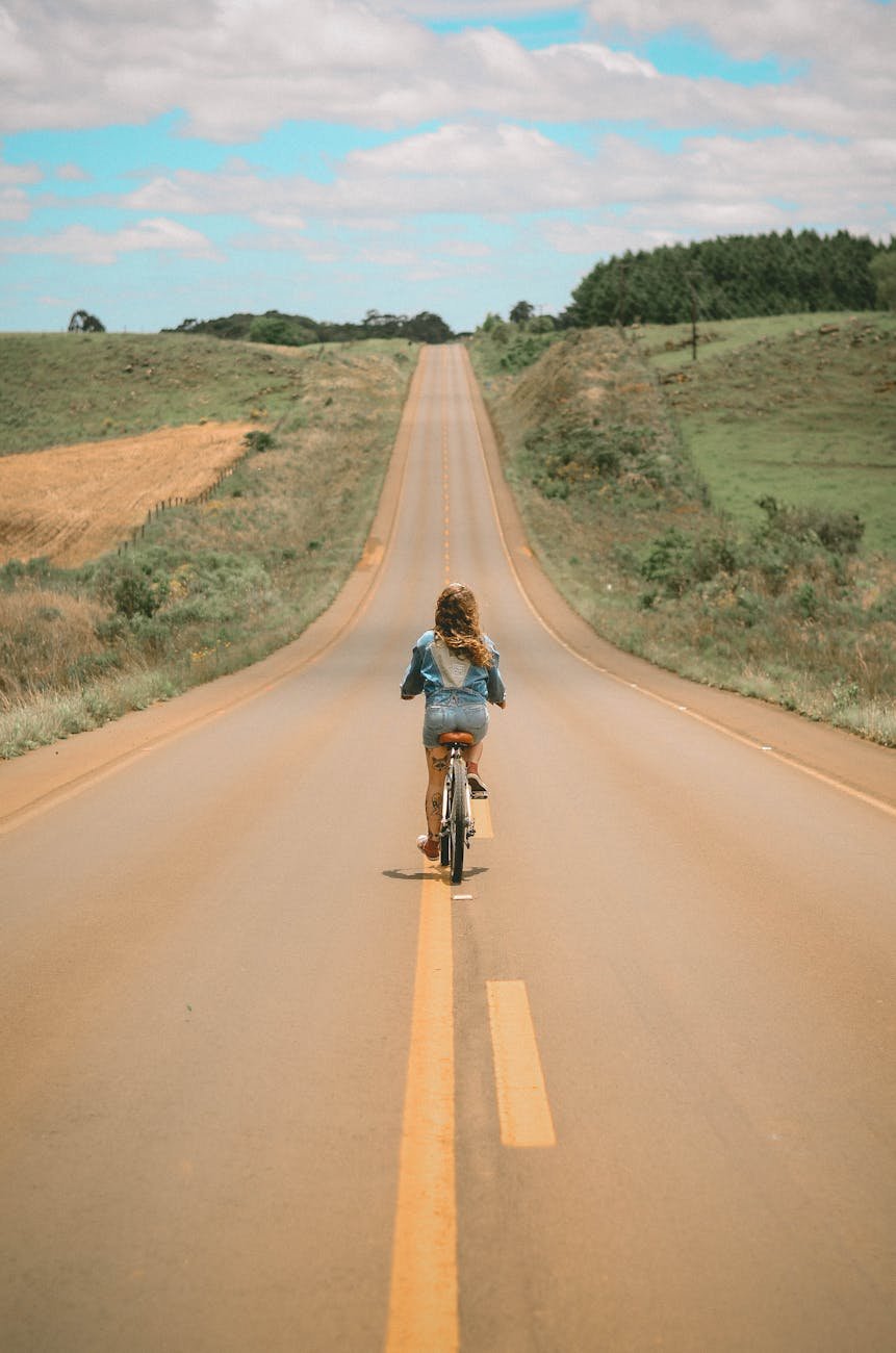 girl riding bike in the middle of the road during day